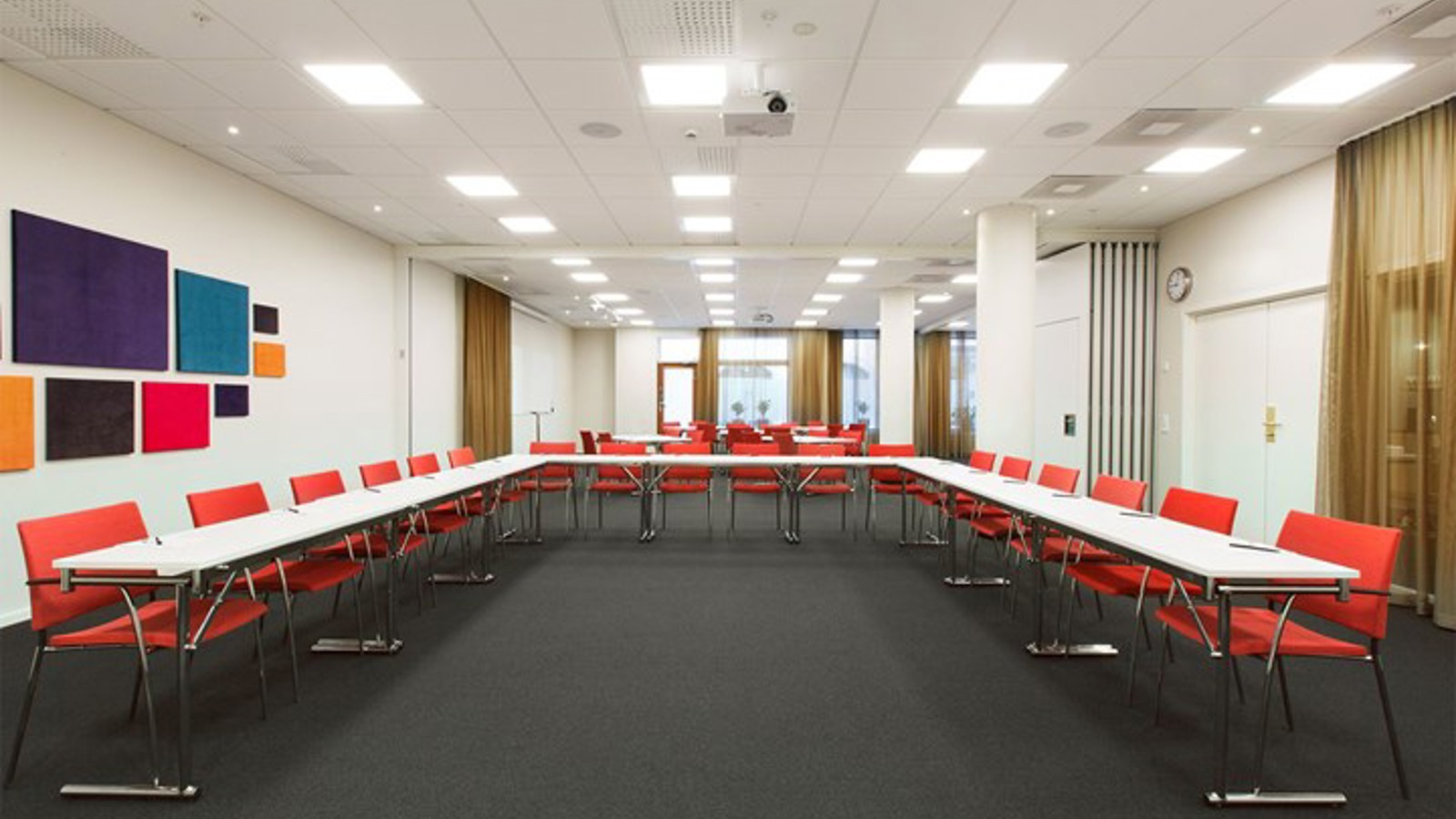 Konferensrum med u-sittning, svart golv, vitt bord, röda stolar