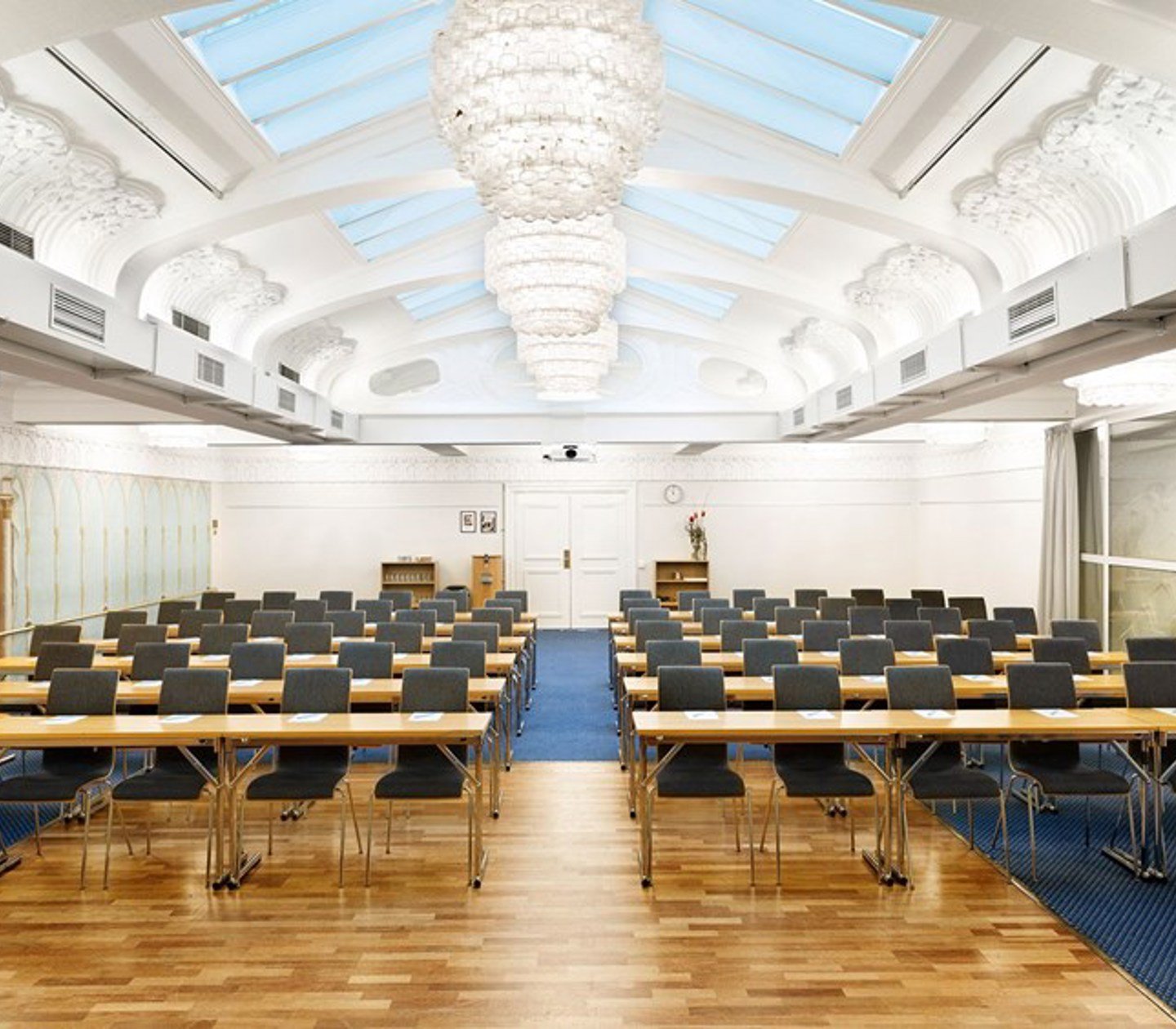 Stor och ljus konferenssal med skolsittning, takfönster, stuckaturer och trägolv