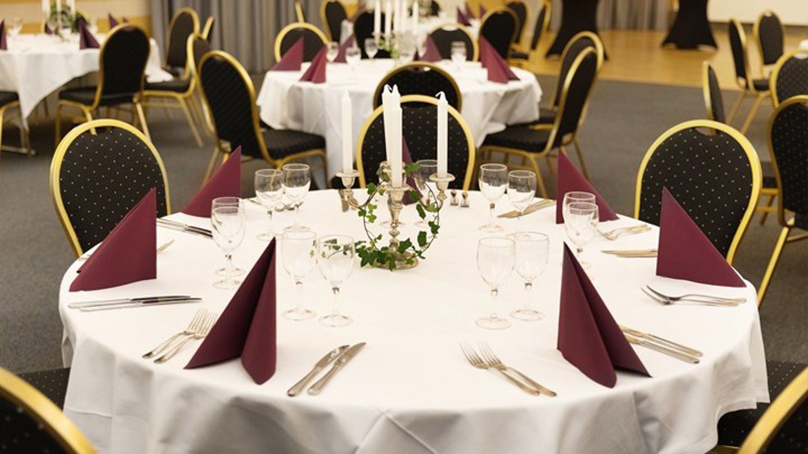 Festlokal med runda bord, vita dukar, glas, bestick och stearinljus