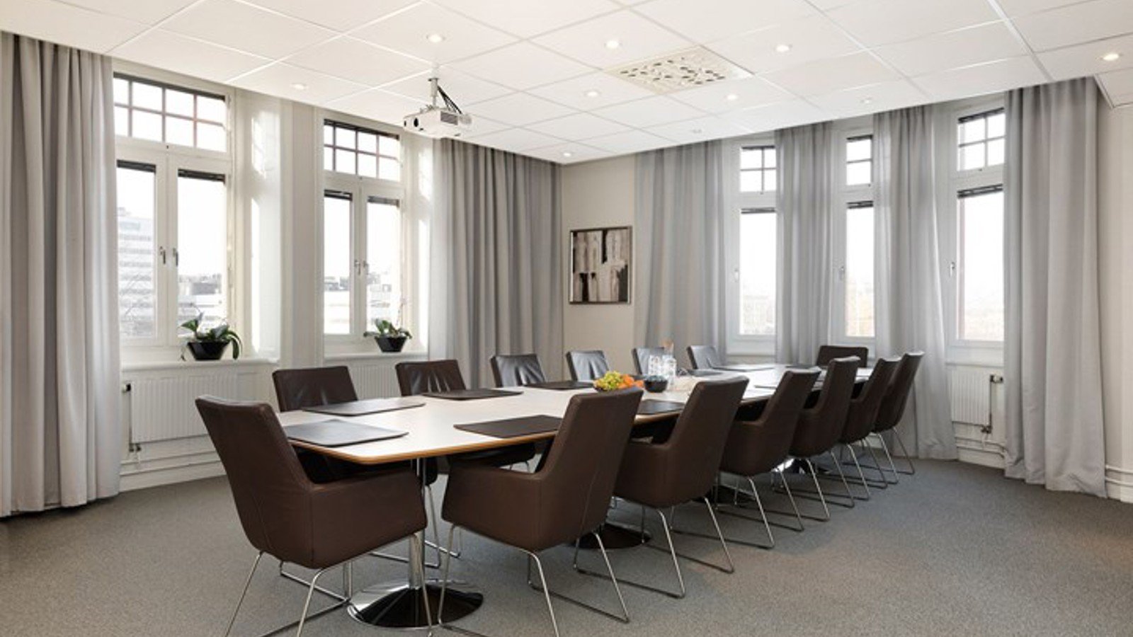 Konferensrum med styrelsesittning, stora fönster, grå gardiner