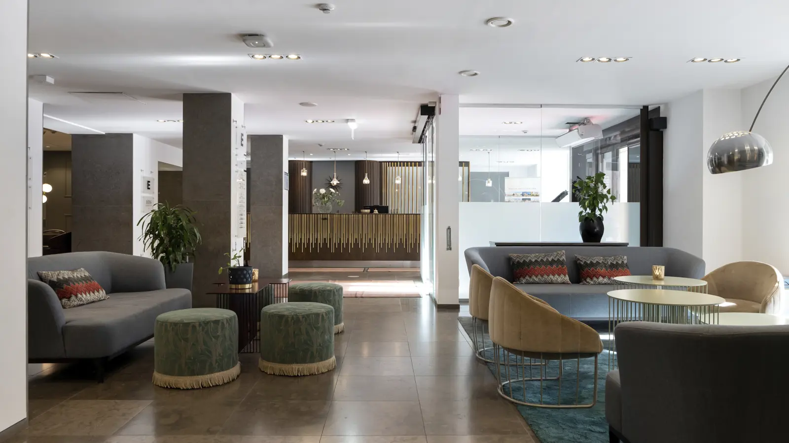 Modern hotel lobby with stylish seating, including sofas and upholstered stools, contemporary lighting, and front desk area with decor.