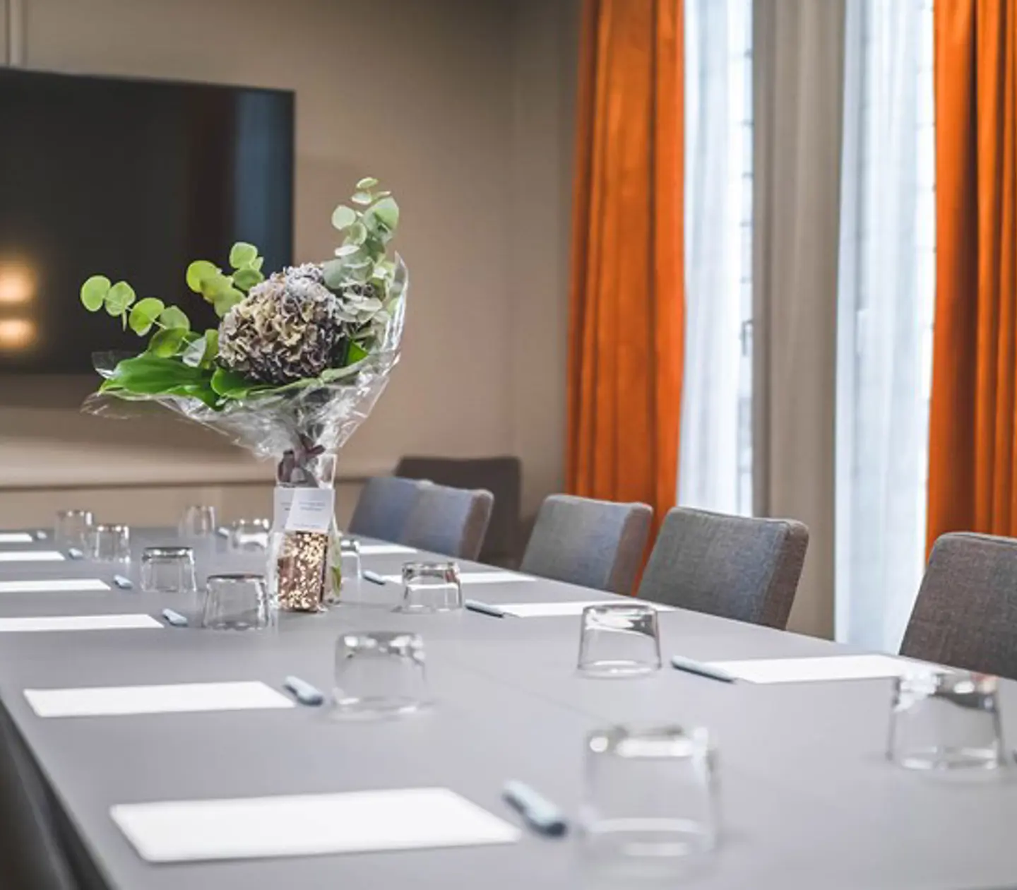 Konferensrum med styrelsesittning, grått bord, grå stolar, rostbruna gardiner