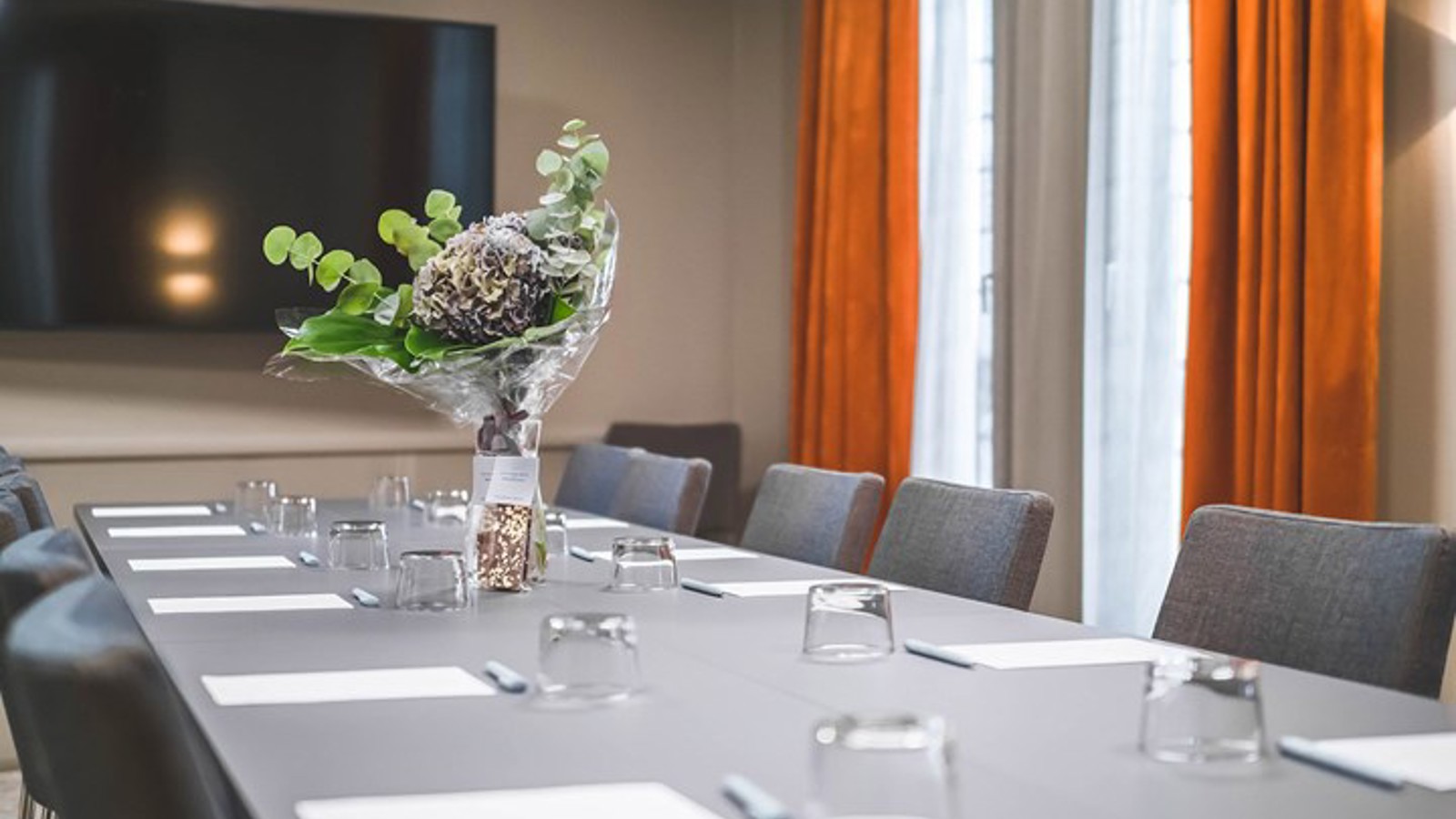 Konferensrum med styrelsesittning, grått bord, grå stolar, rostbruna gardiner