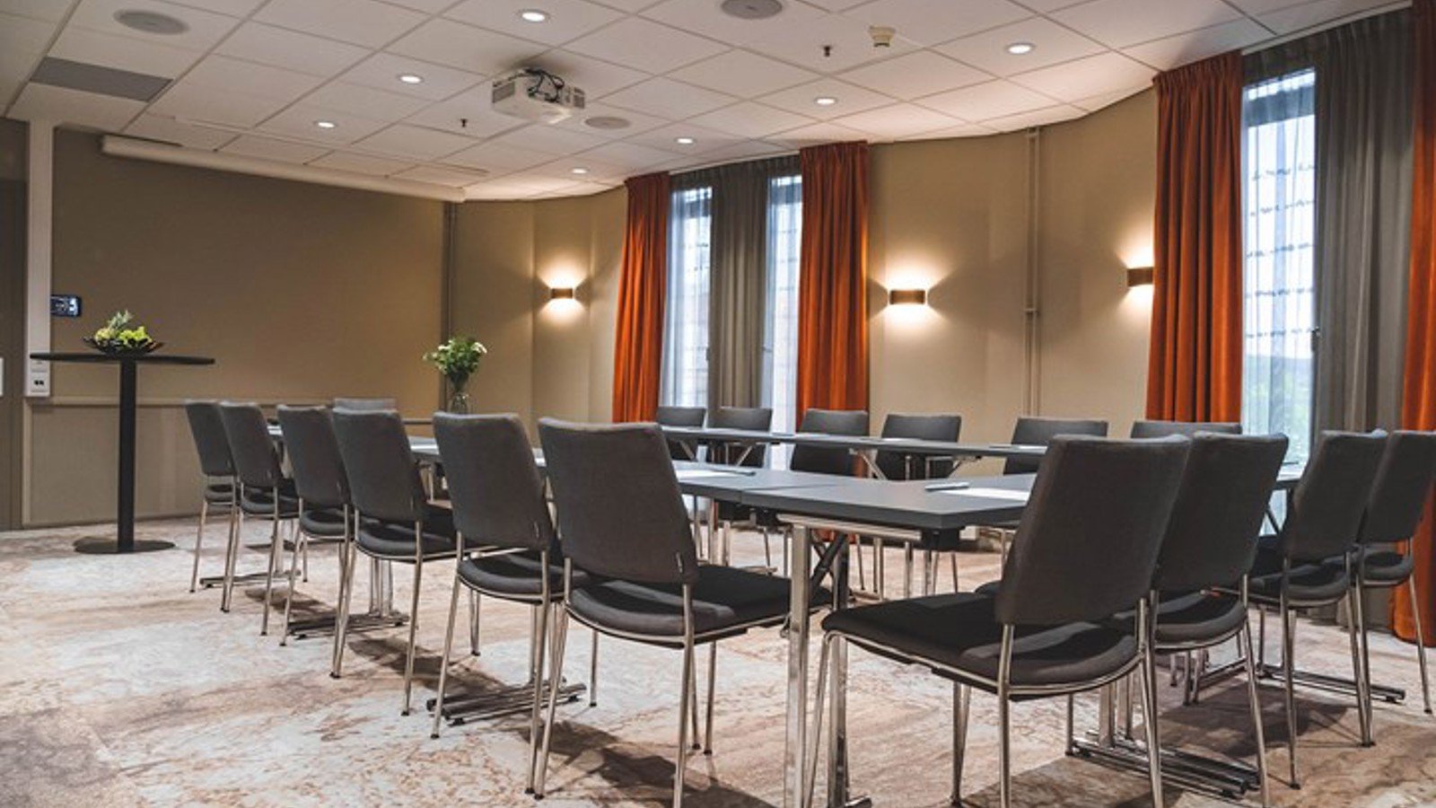 Konferenslokal med u-sittning, grå stolar och röda gardiner