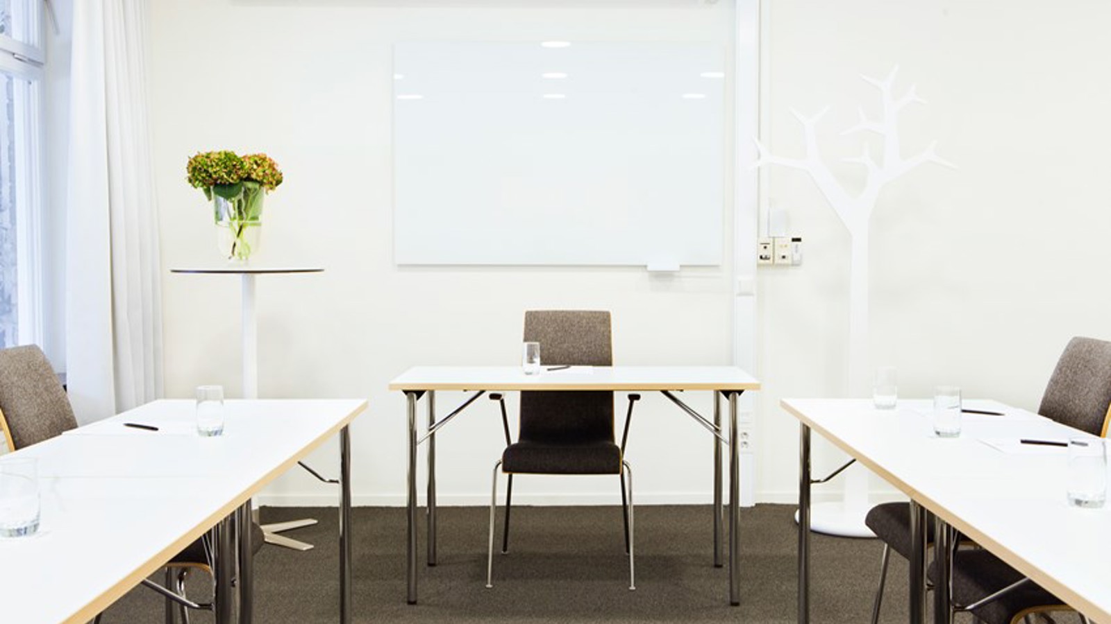 Konferensrum med u-sittning, vita bord, vita väggar och grå matta