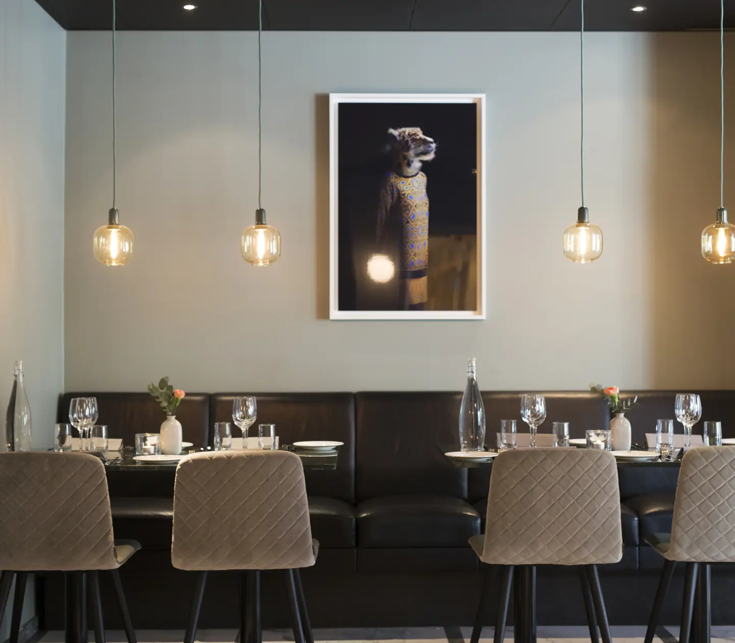 Modern restauranginteriör med fyra stolar vid ett dukat bord, hängande lampor och en tavla på väggen.