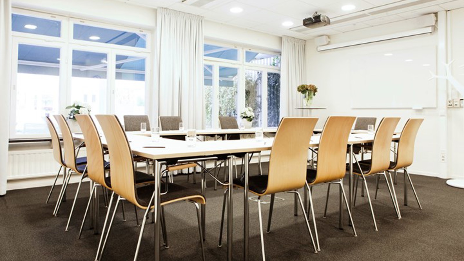 Conference room with u-shaped seating, white walls, large windows and gray carpet