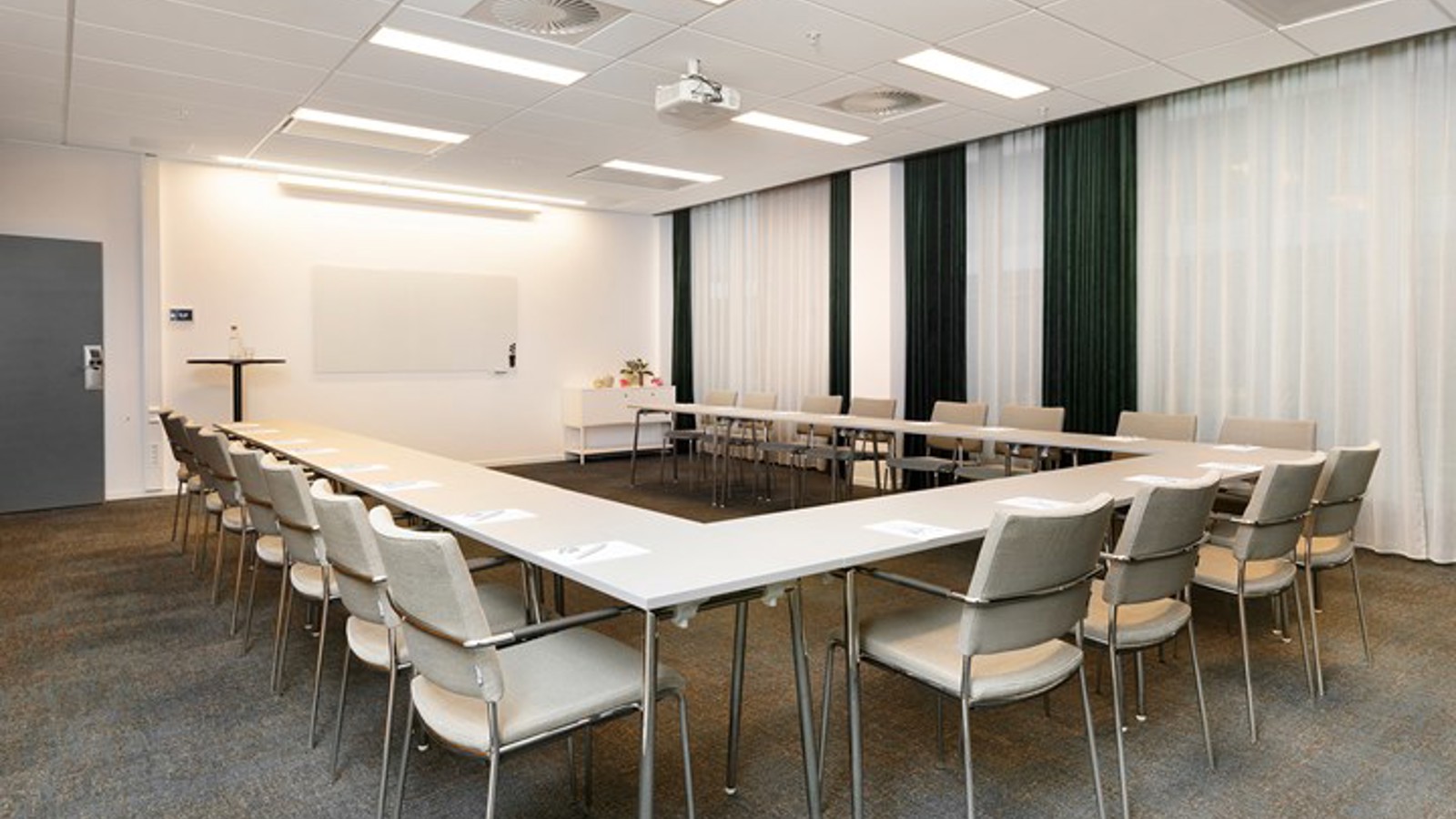 Conference room with u-shaped seating, white chairs, white table, gray carpet and draperies