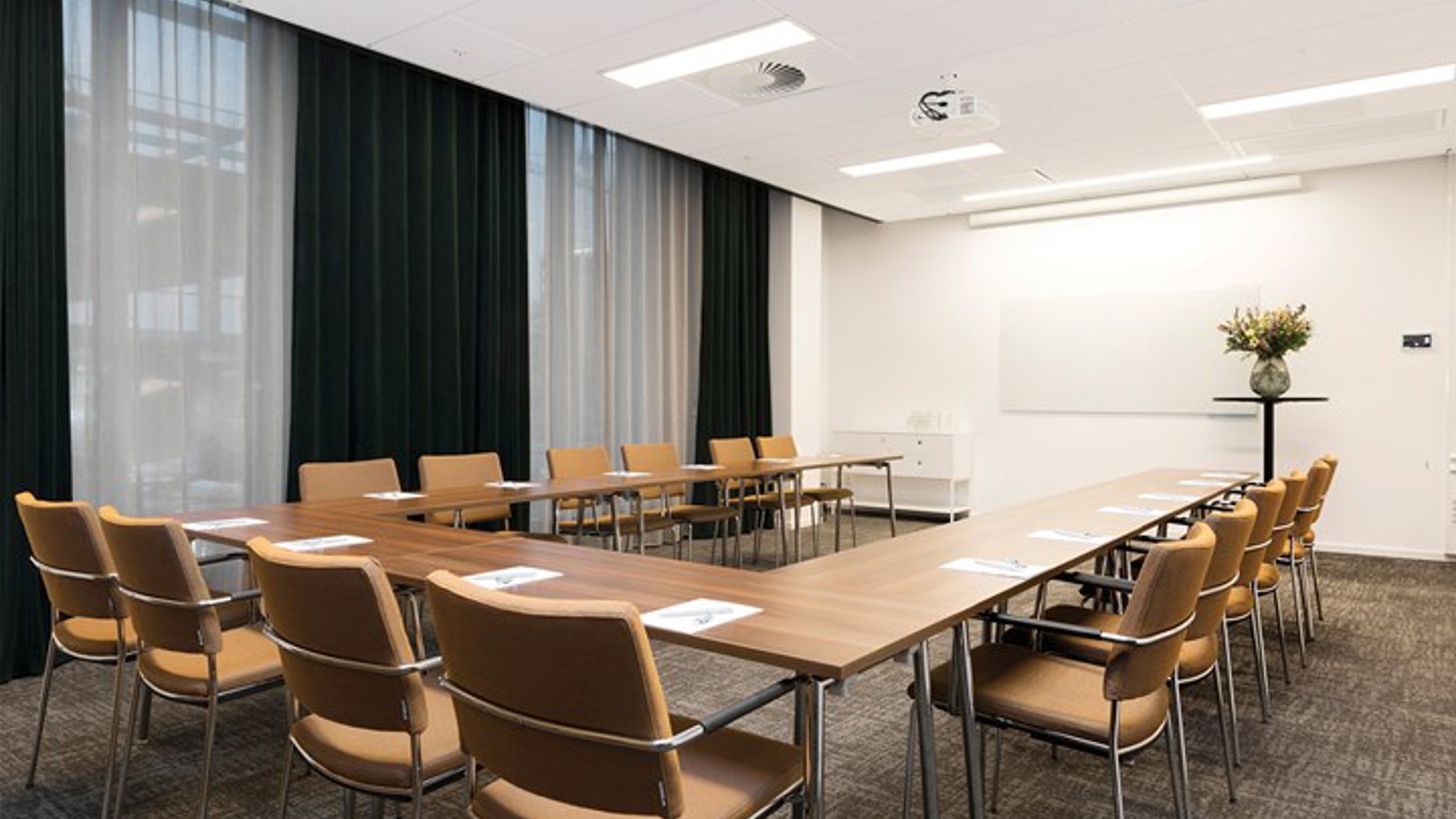 Konferensrum med u-sittning, bruna möbler, vita väggar, grå matta och stora fönster