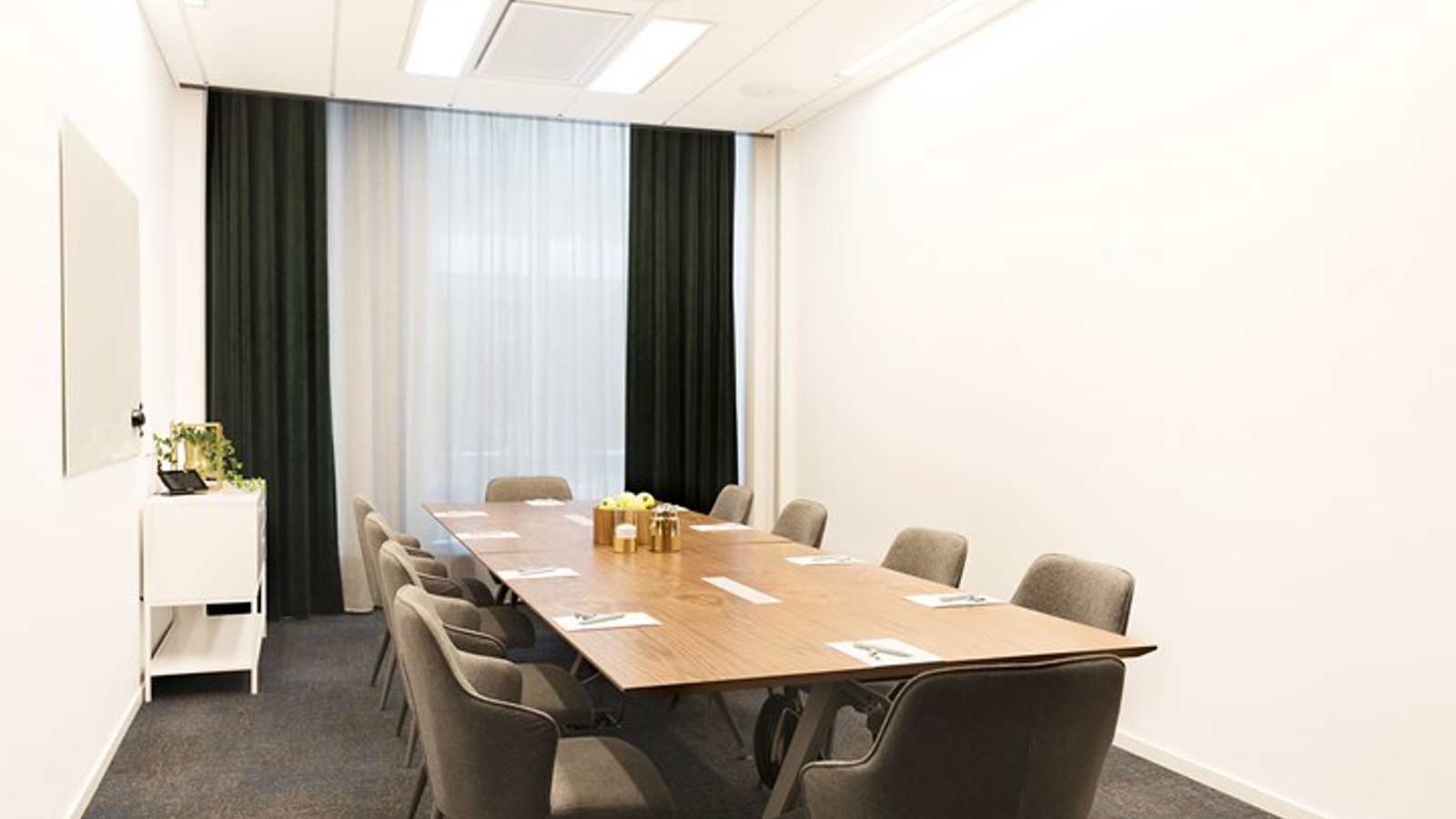 Konferensrum med styrelsesittning, vita väggar, grå matta