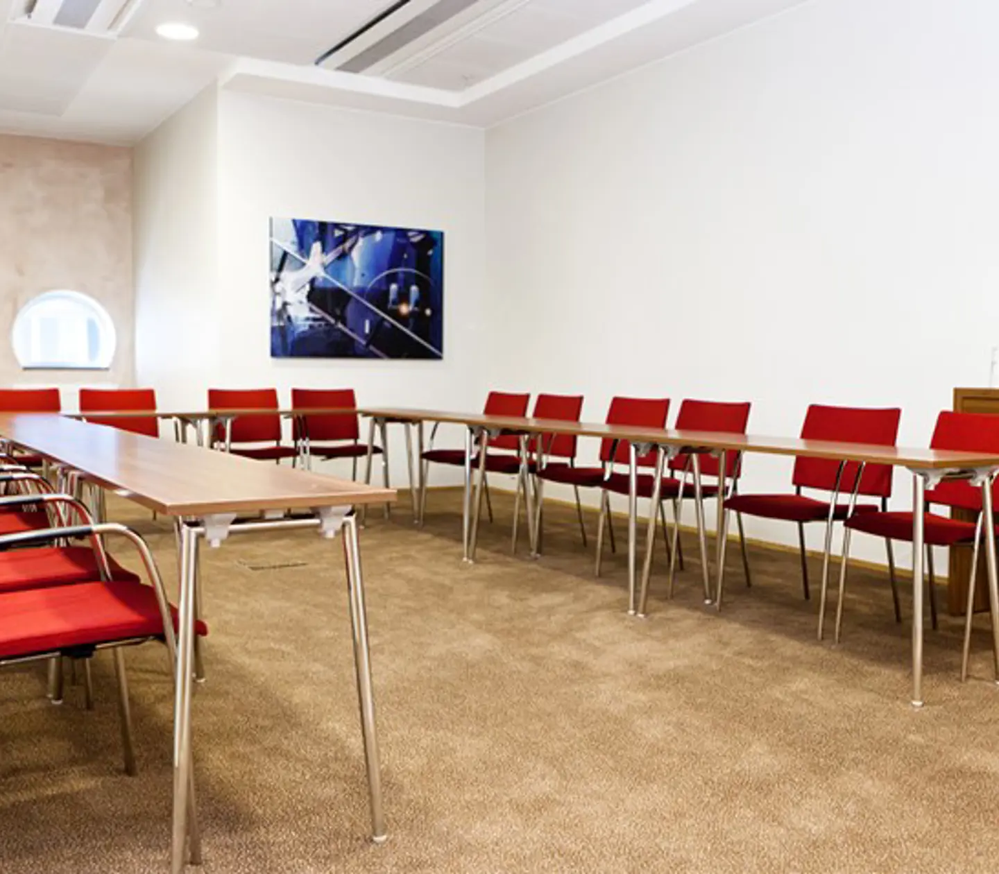 Konferensrum med u-sittning, röda stolar, ljusbrunt golv och vita väggar
