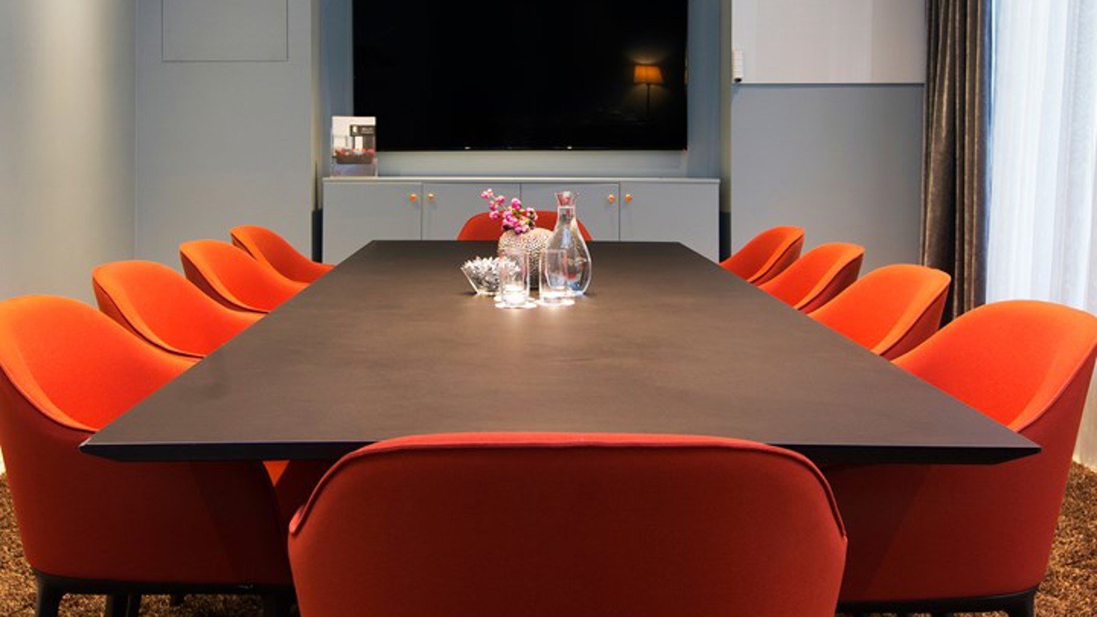 Konferensrum med styrelsesittning, brunt bord, röda stolar och blå väggar