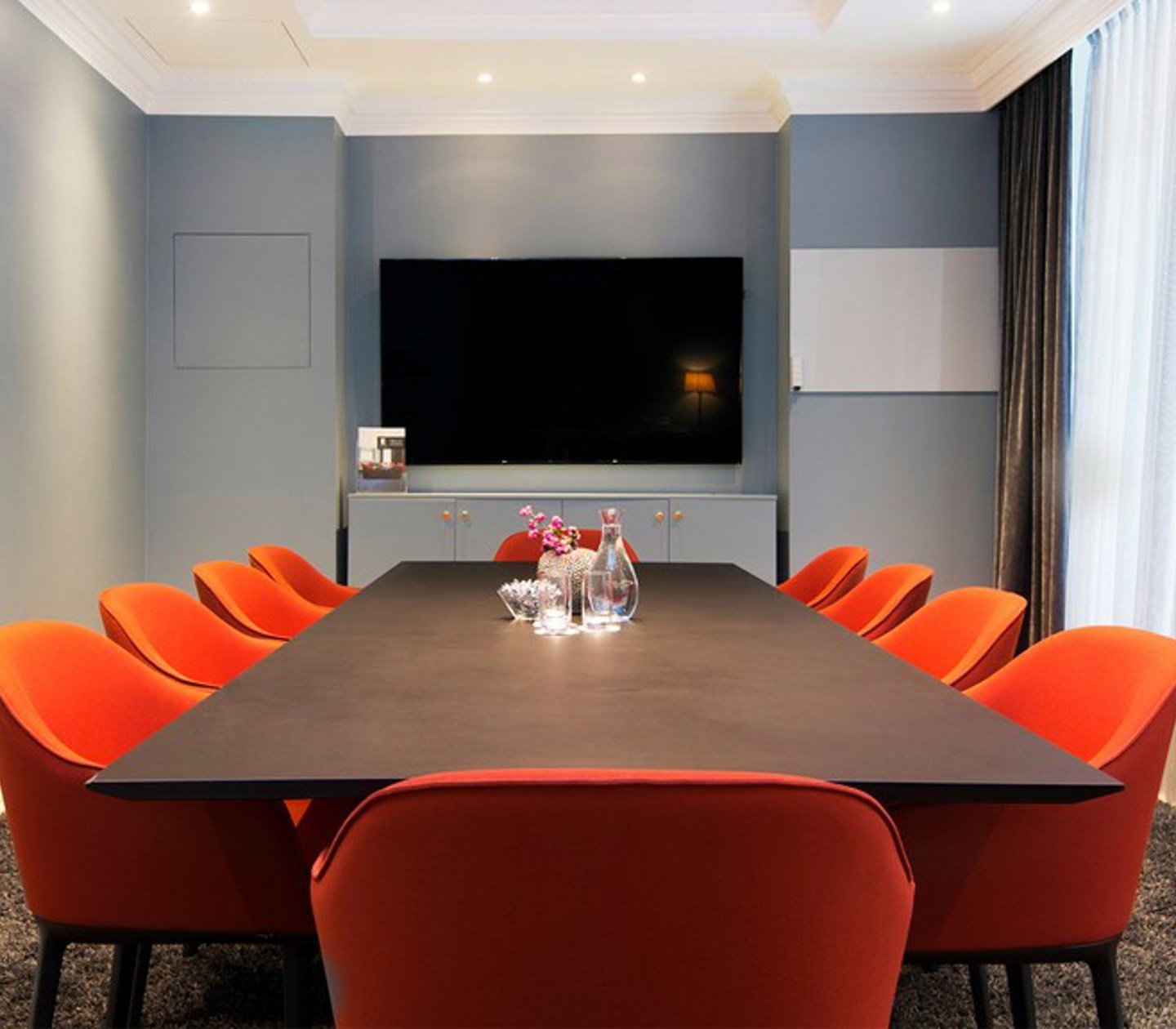Konferensrum med styrelsesittning, mörkbrunt bord, röda stolar och blå väggar