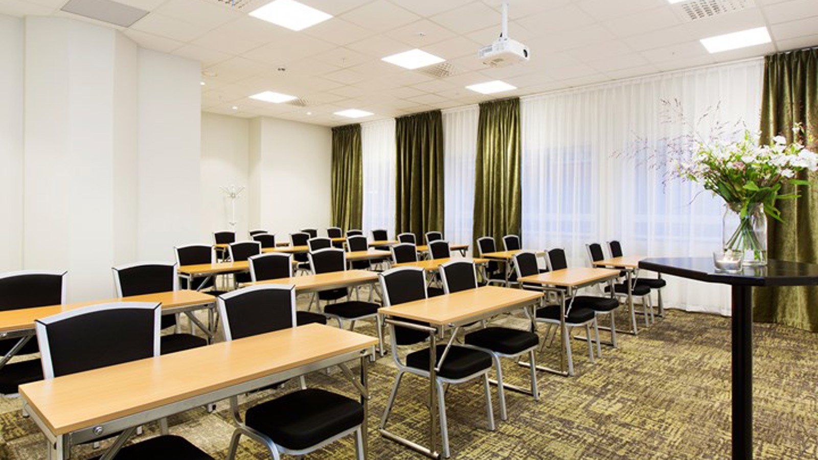 Konferensrum med skolsittning, vita väggar, svarta stolar, träbord