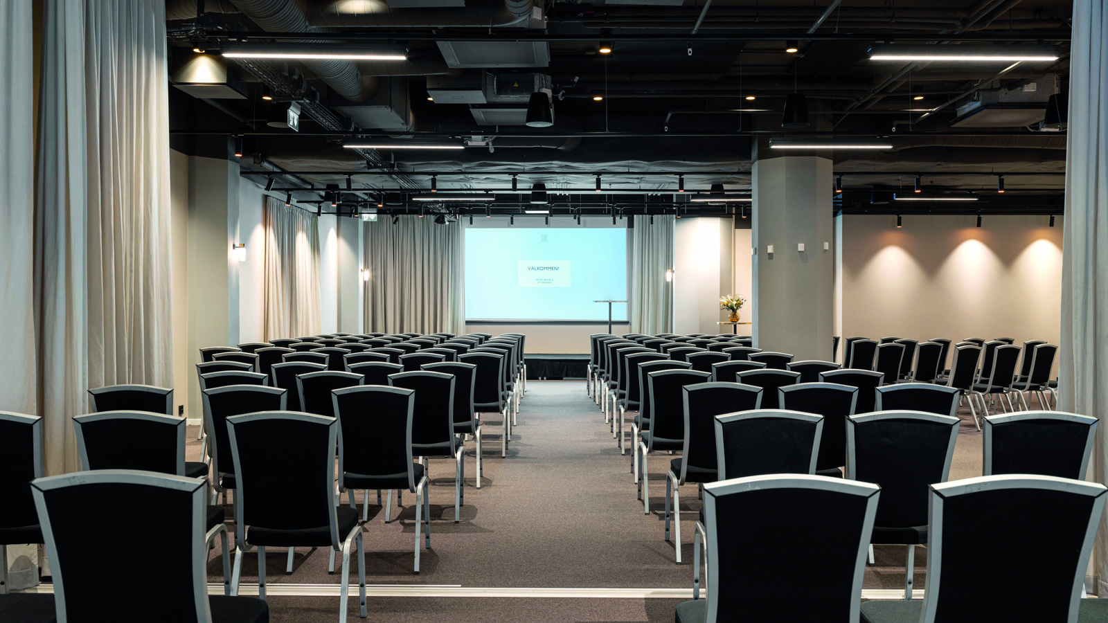 Konferensrum med bio-sittning, mörka stolar och vita väggar