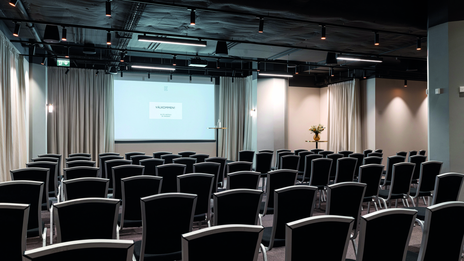 Konferensrum med biosittning, grå stolar, vita väggar och projektor