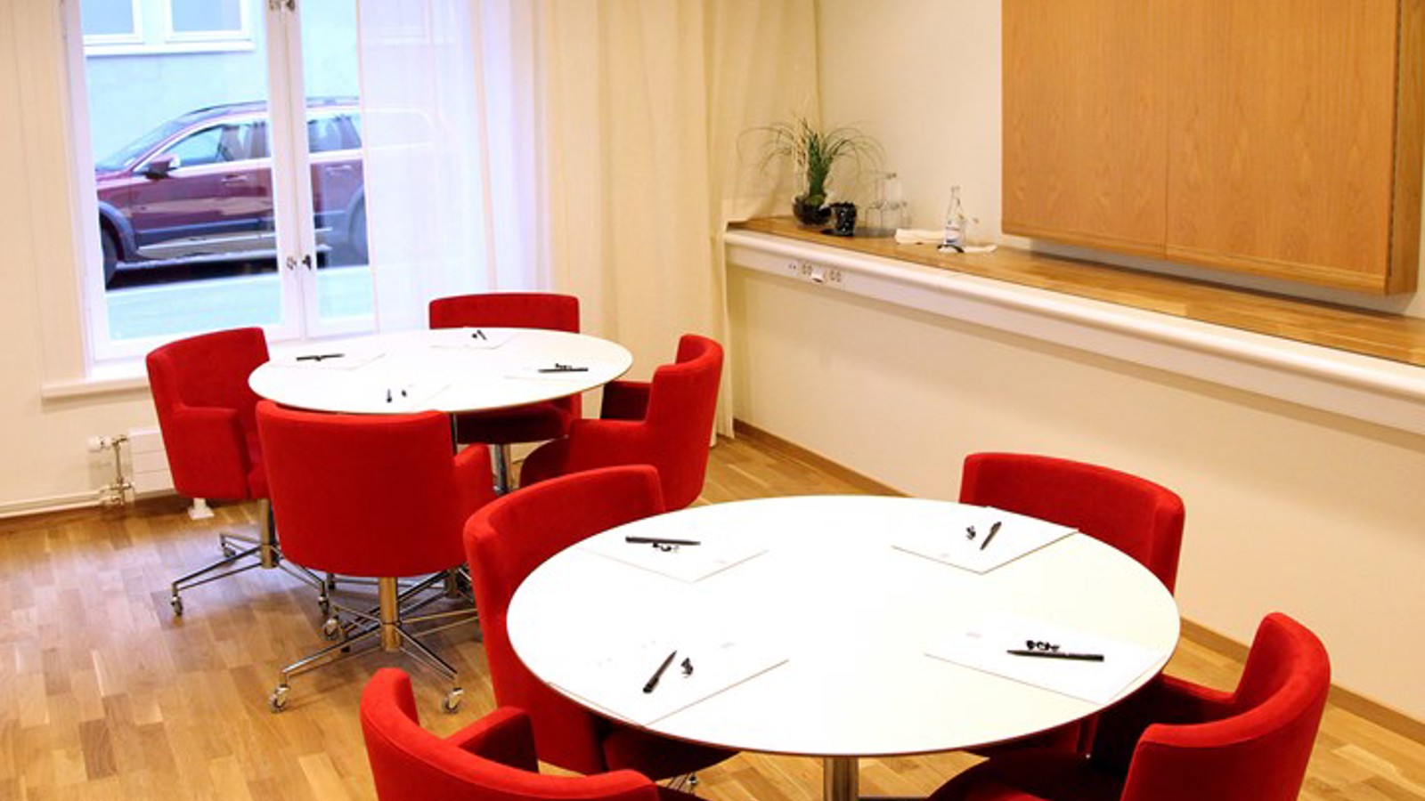 Ljust konferensrum med vita bord och röda stolar uppställda som öar