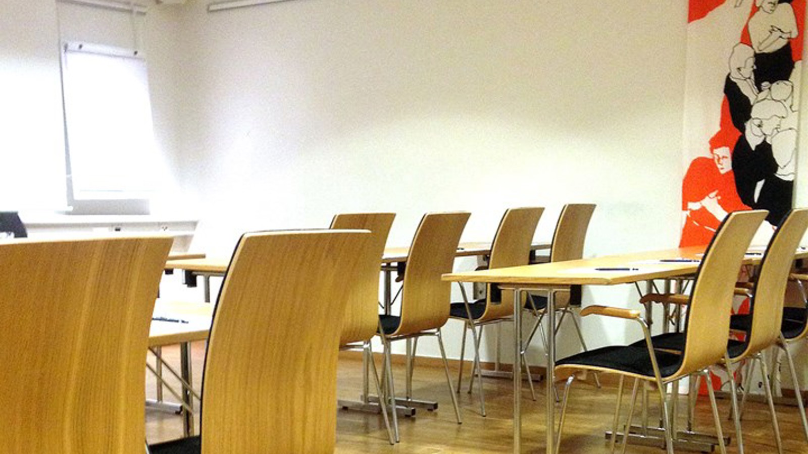 Ljust konferensrum i skolsittning med trägolv och vita väggar