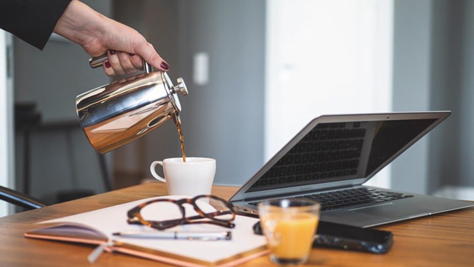 Detaljbild på hand som häller upp kaffe, med uppslagen bok och laptop i förgrunden