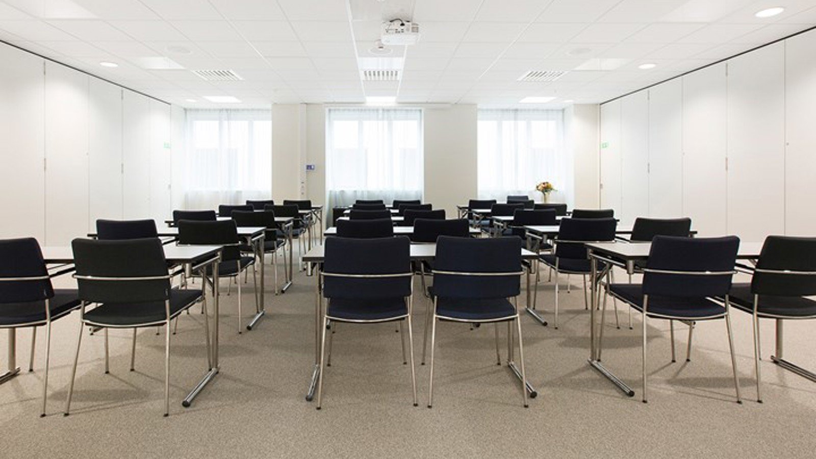Konferensrum med skolsittning, vita väggar och tak, svarta stolar
