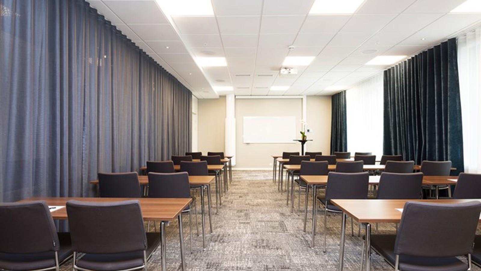 Konferensrum med skolsittning, grå stolar, grått golv och grå draperier