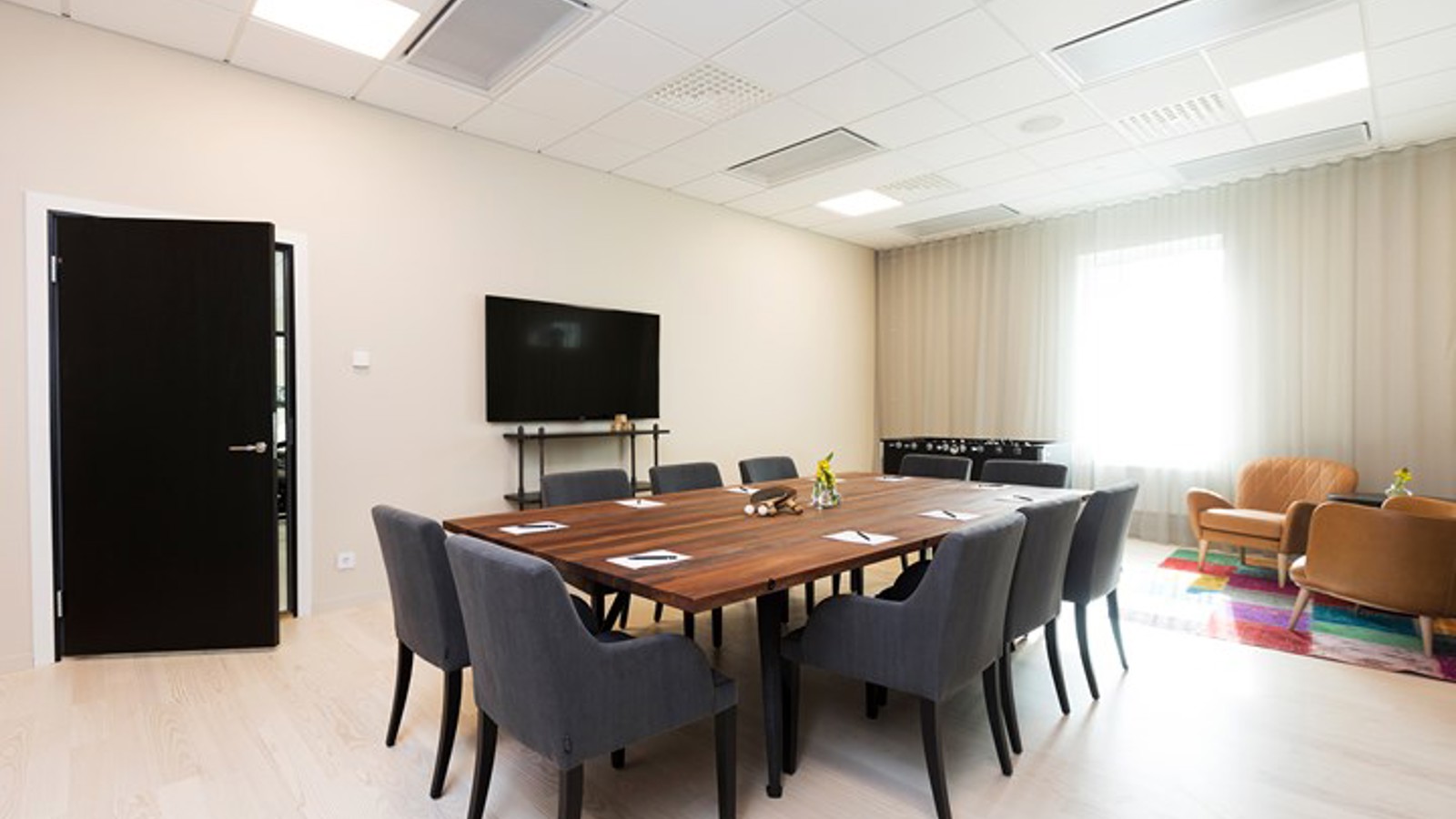 Konferensrum med styrelsesittning, brunt bord, grå fåtöljer och ljusa väggar