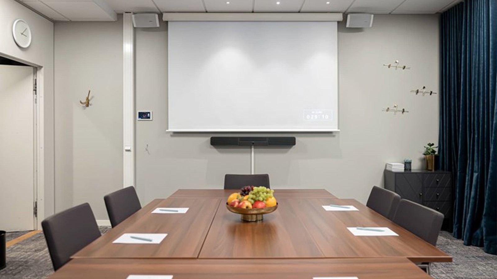 Konferensrum med brunt bord, grå stolar, ljusa väggar och projektor
