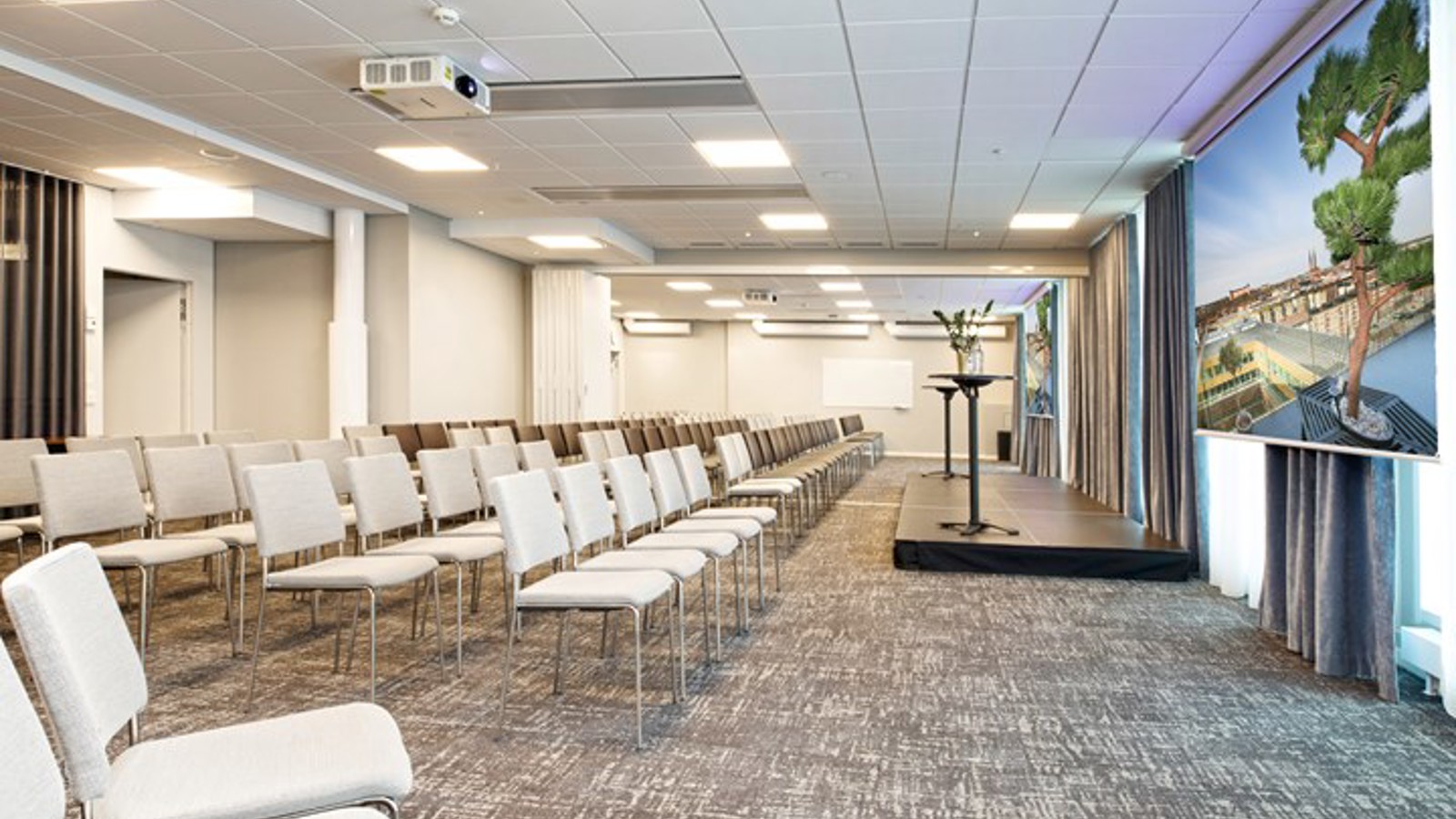 Konferensrum med biosittning, grått golv, vita stolar och vita väggar