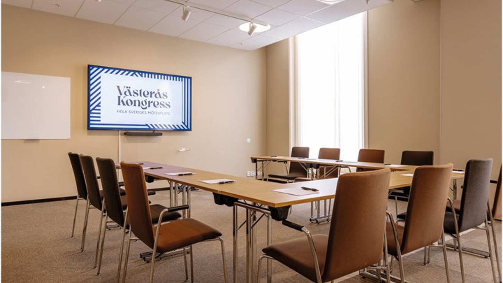 Konferensrum i ljusbruna färger med u-sittning, skärm och stort fönster