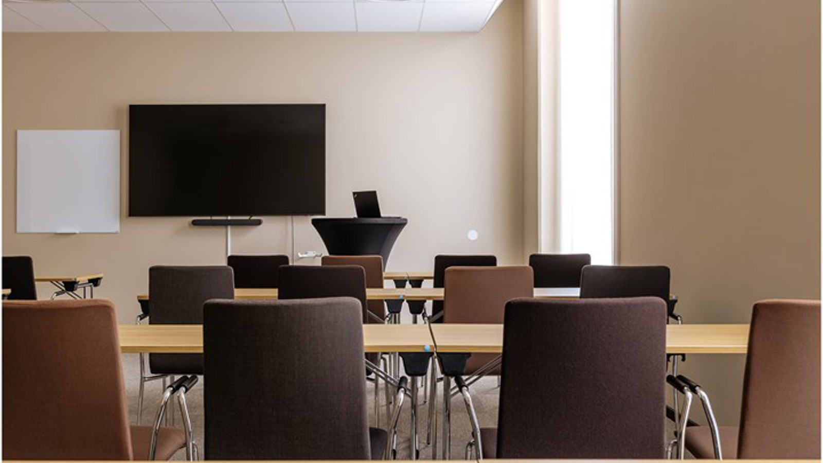 Konferensrum med skolsittning i ljus- och mörkbruna färger med tv-skärm och fönster