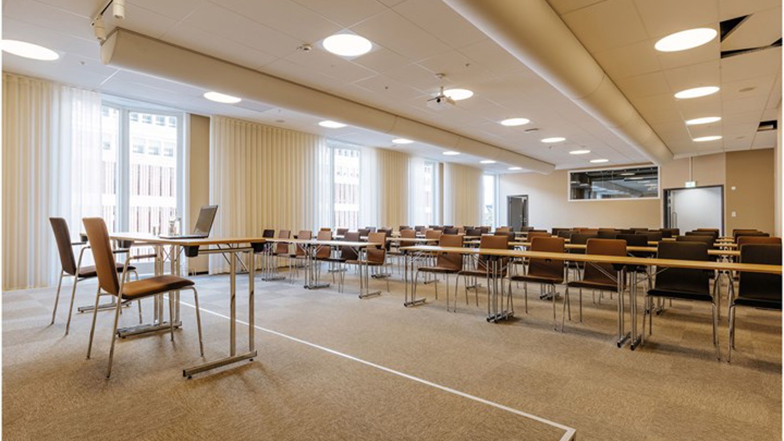 Konferenslokal i skolsittning, med scen och stora fönster