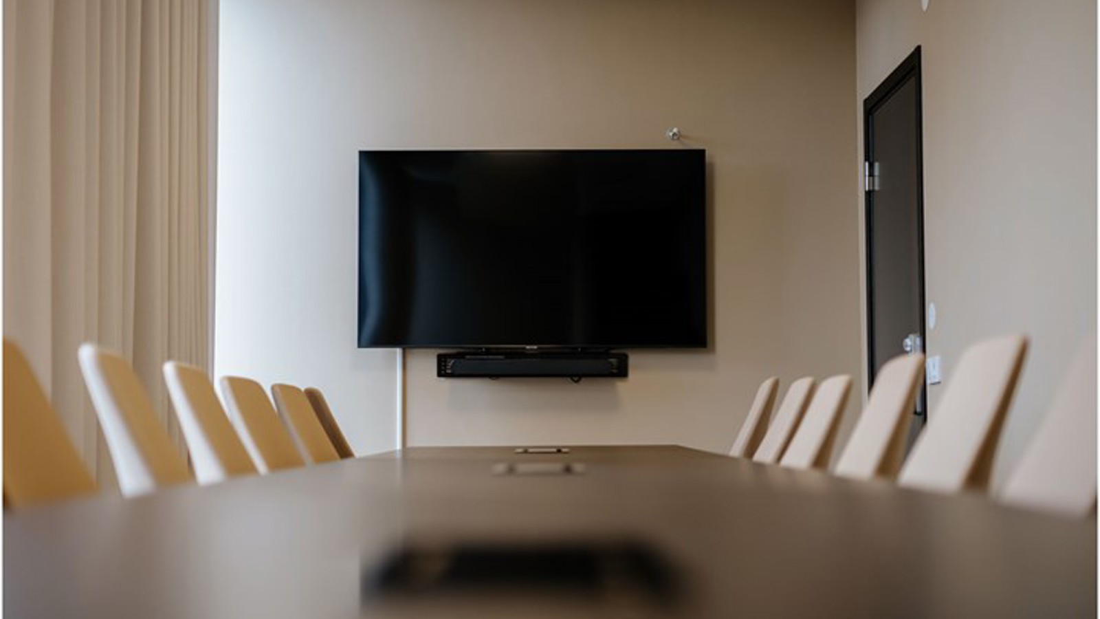 Konferensrum med styrelsesittning, brunt bord och tv-skärm