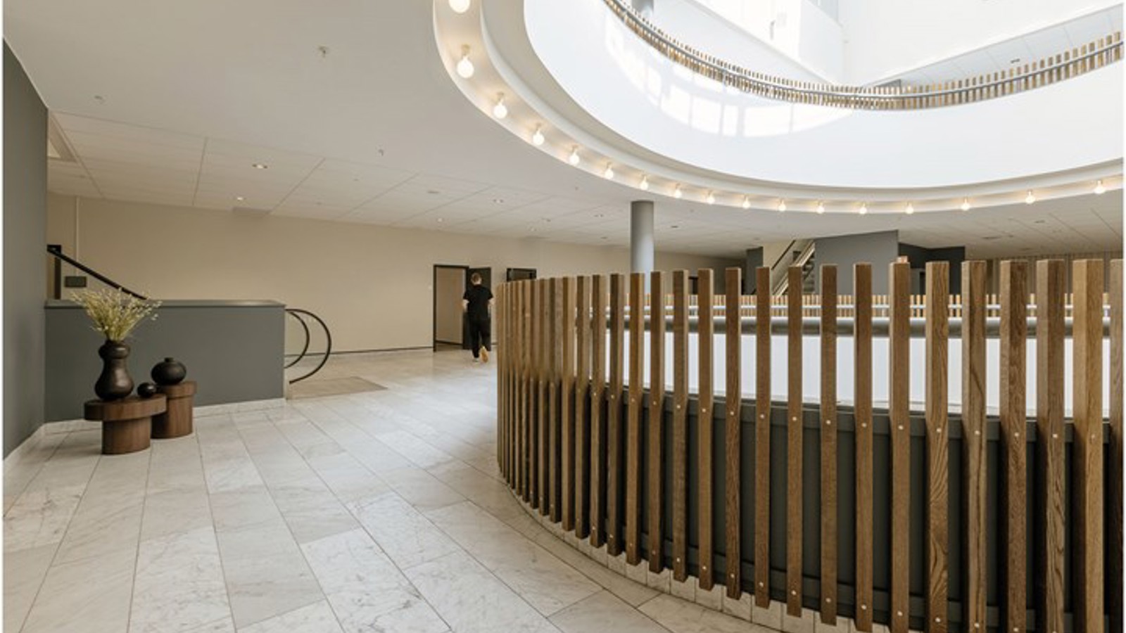Open indoor area with wood paneling, light stone floor, round skylight and escalator