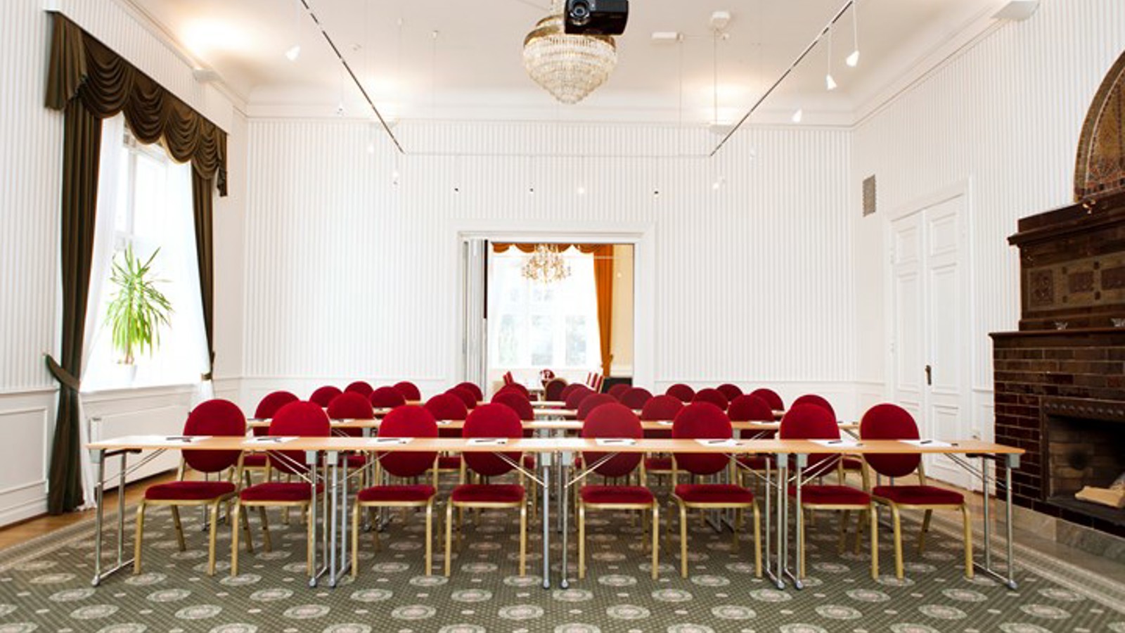 Konferensrum med skolsittning, röda stolar, vita väggar och grönmönstrad matta