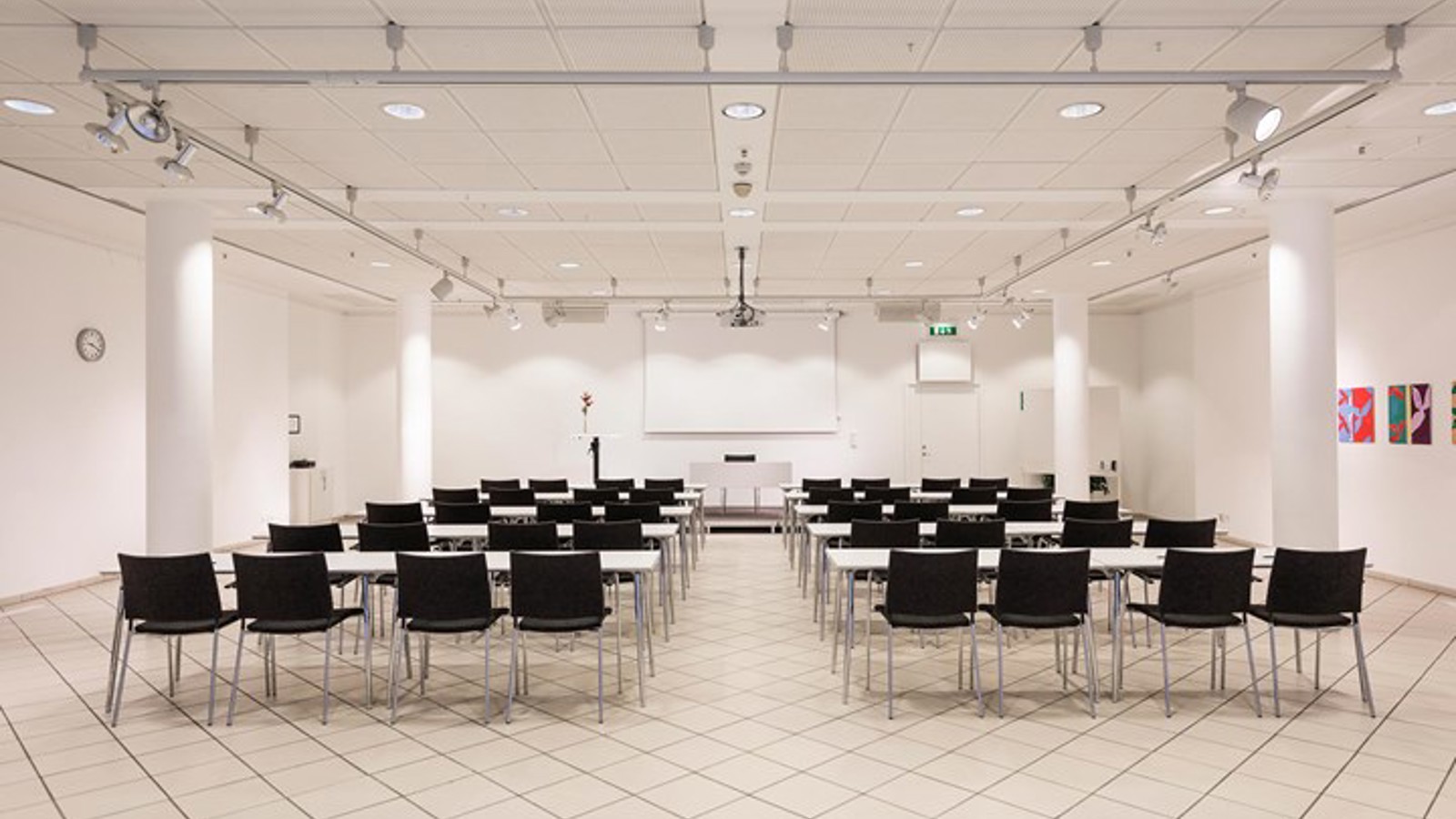 Konferenslokal med vita väggar, vitt golv och svarta stolar placerade i biosittning