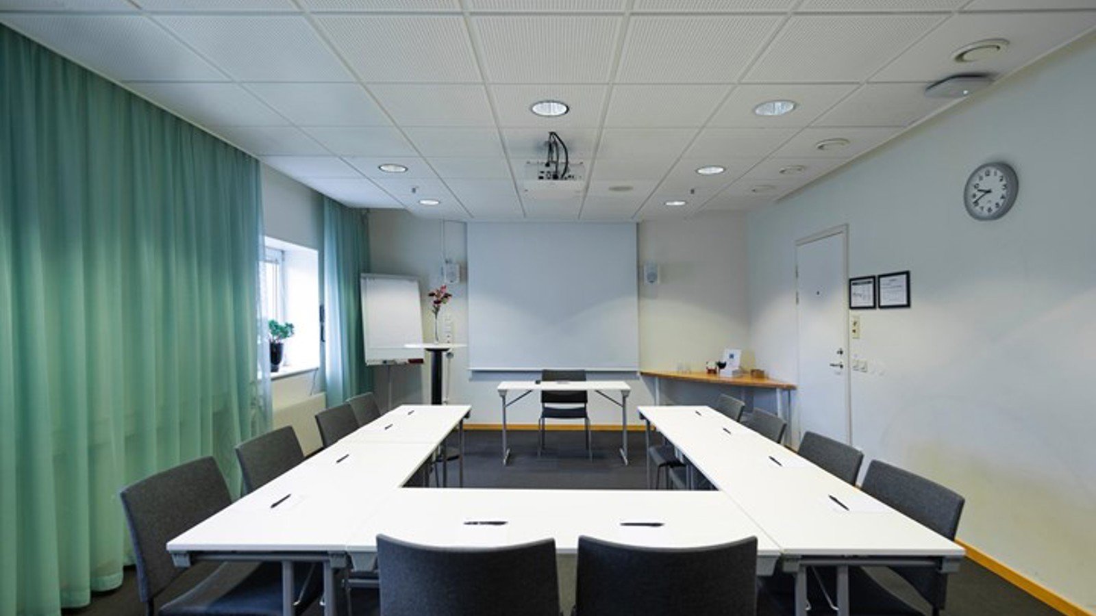 Konferensrum med u-sittning, gröna gardiner, vitt bord, grå stolar