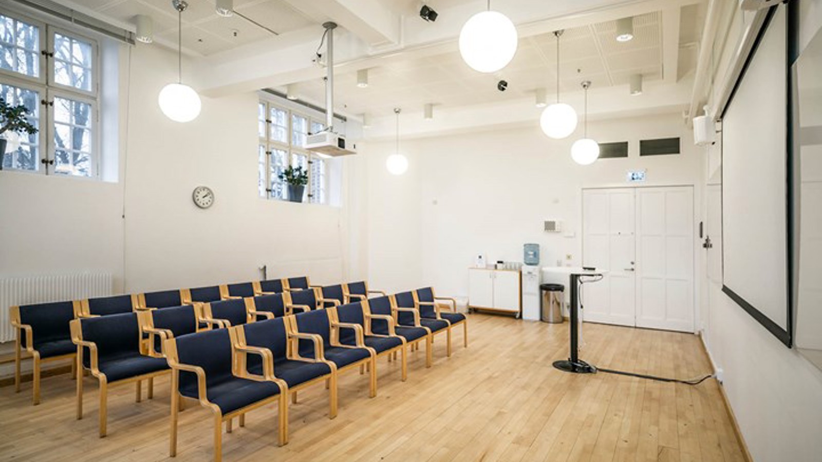Ljus konferenslokal med mörka stolar i biosittning, projektor och stora fönster
