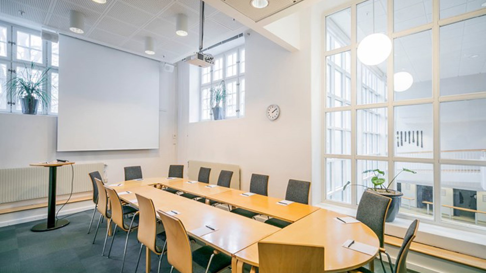 Konferensrum med styrelsesittning, vita väggar, träbord och blå matta