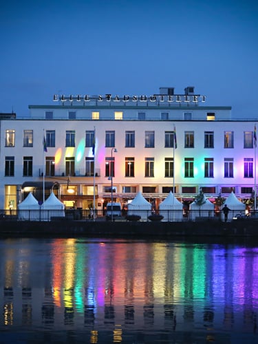 En magnifik byggnad lyser upp i regnbågsfärger som speglar sig i sjön