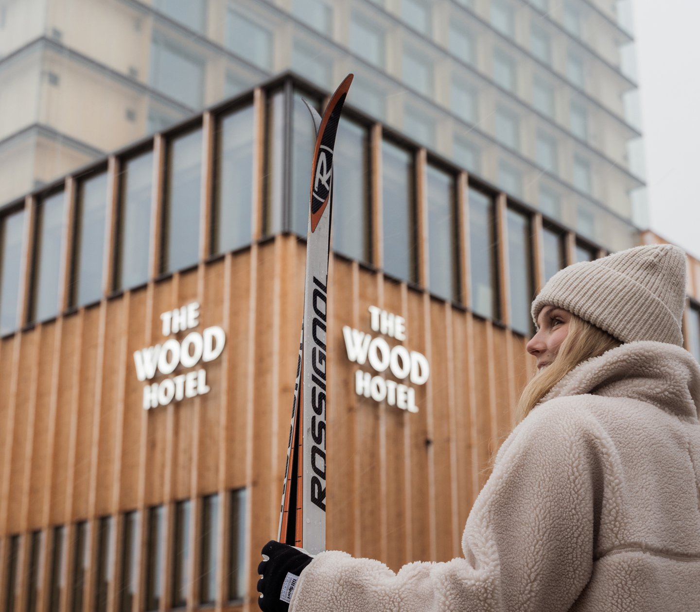 Kvinna i vinterkläder med skidor i handen framför The Wood Hotel