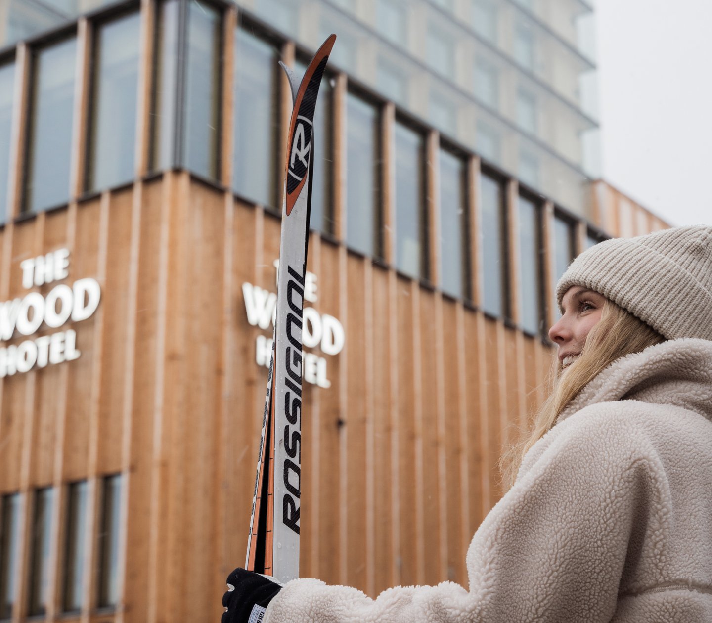 Kvinna som står utanför hotell med skidor i händerna