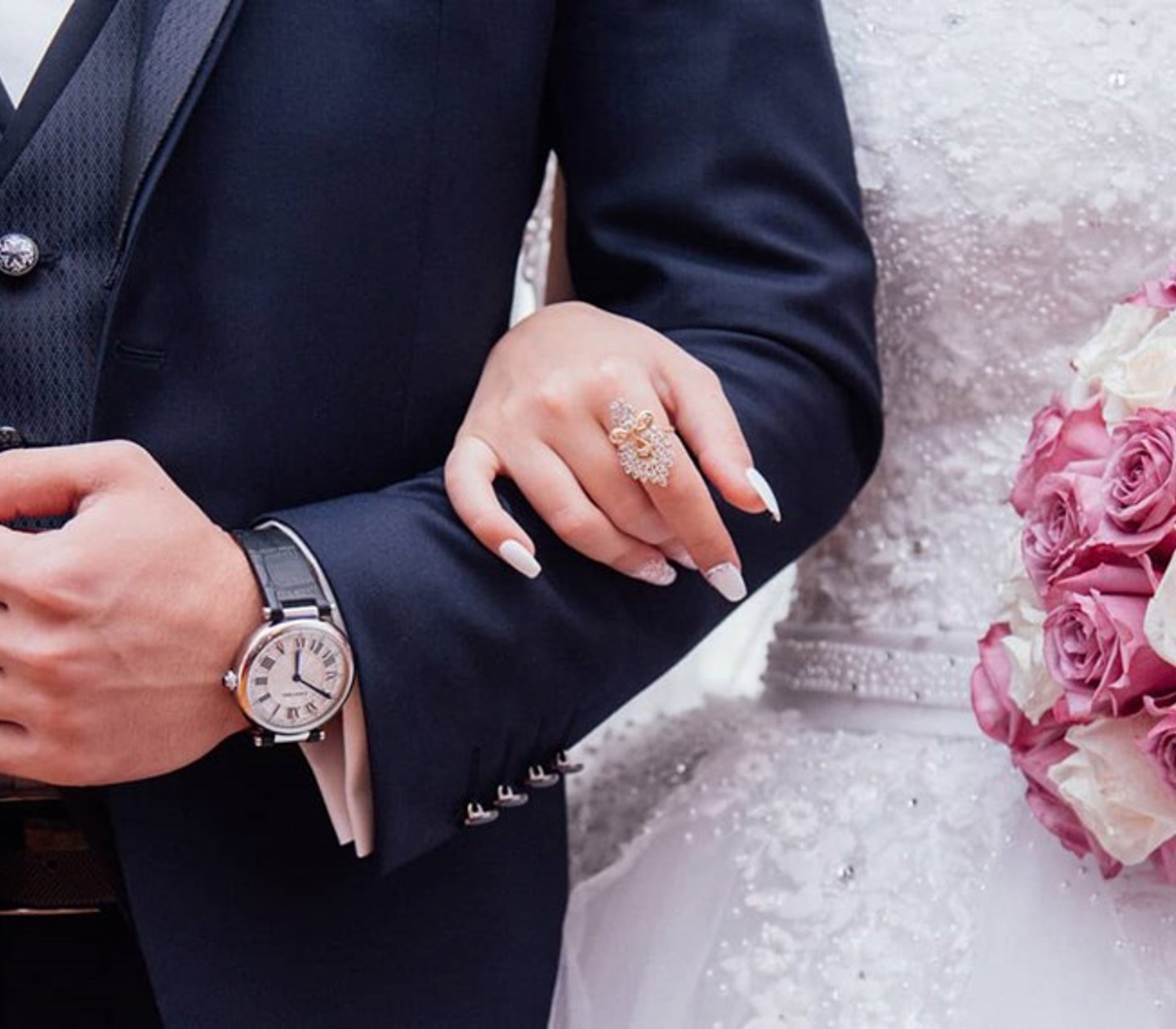 En kvinna i bröllopsklänning håller ena handen runt sin man och en bukett i den andra handen.