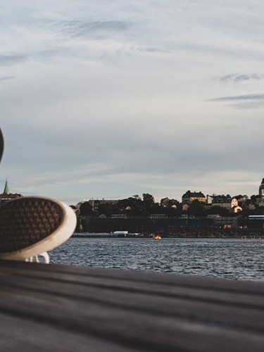 En person sitter på en brygga och håller en mobil med utsikt över Stockholm