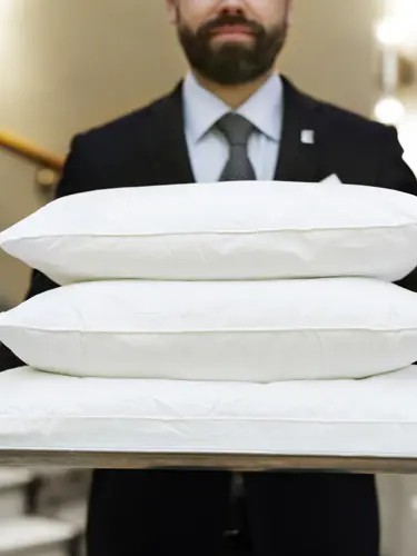 Man i kostym som bär tre vita kuddar på bricka