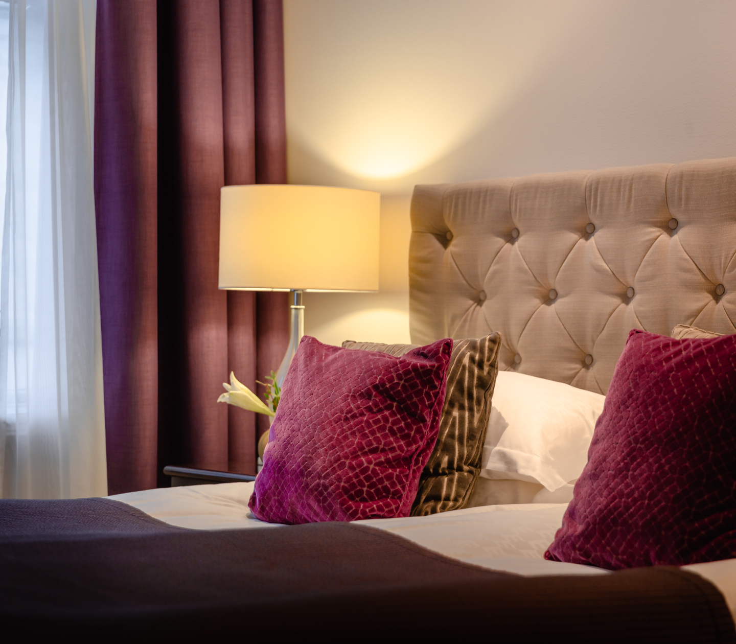 Mysigt hotellrum med säng, lila kuddar och sänglampa