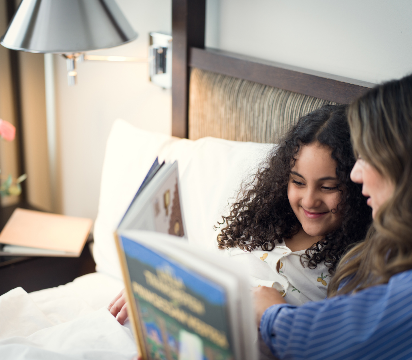 Mother and daughter reading book in hotel bed