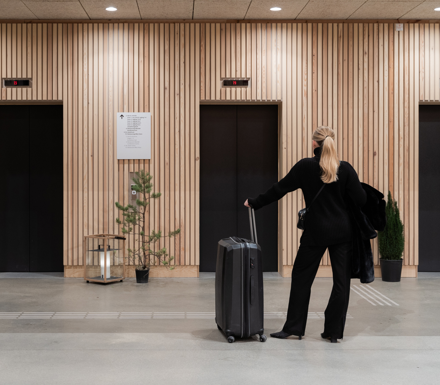 Kvinna med resväska som står framför tre hissdörrar