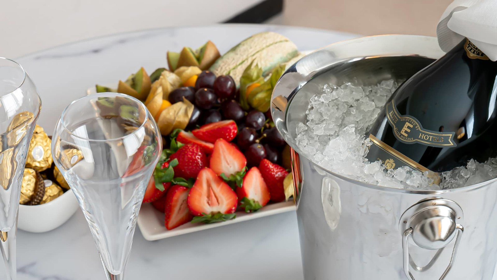 Champagne in an ice bucket, two glasses, chocolate and fruit platter on display