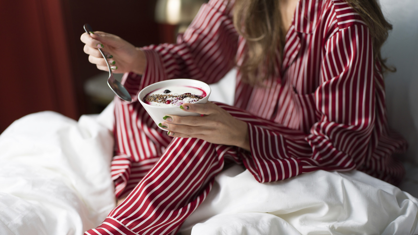 Girl in red and white striped pajamas eating breakfast in hotel bed