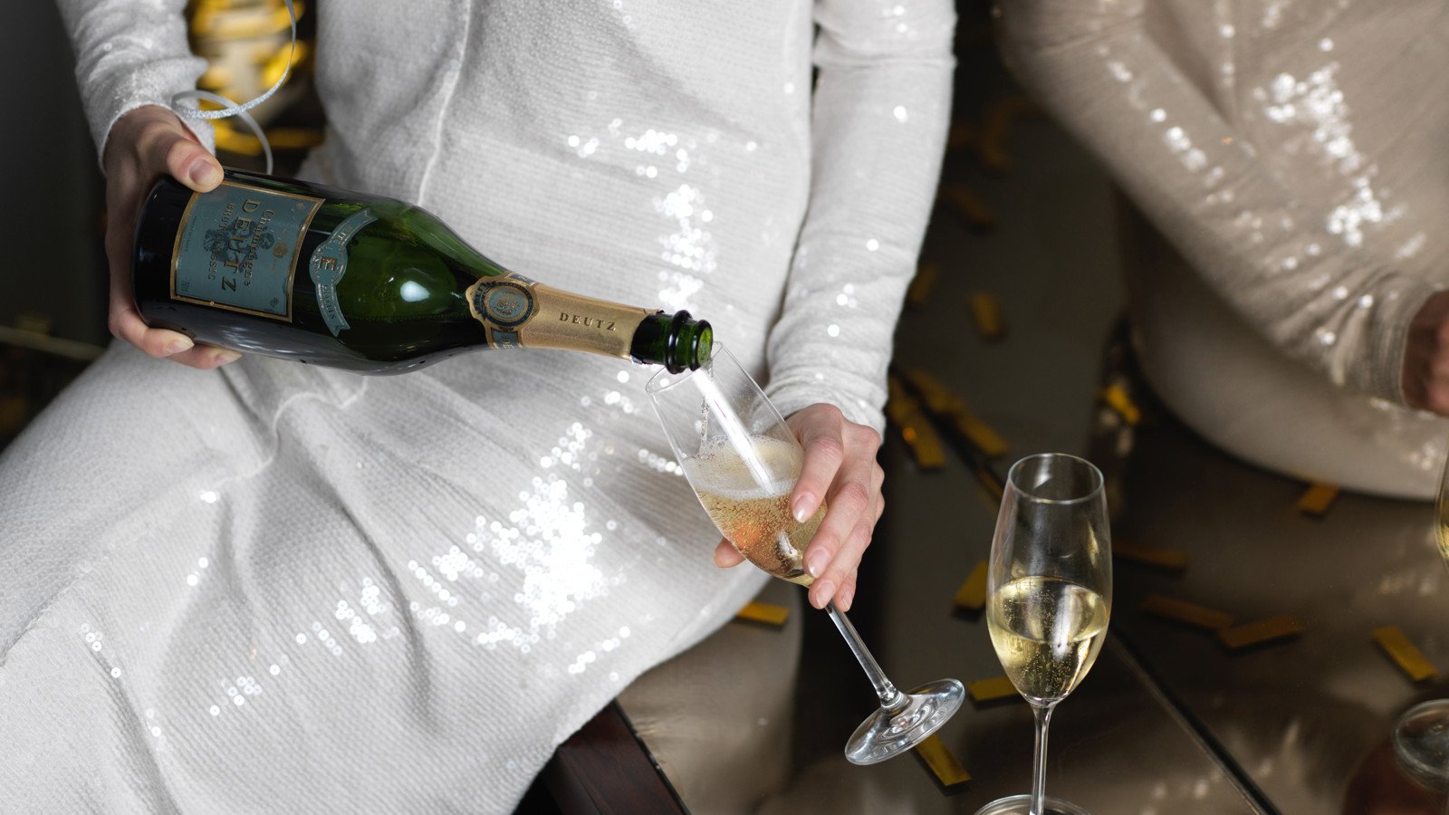 Kvinna i silvrig klänning häller upp Champagne i ett champagneglas